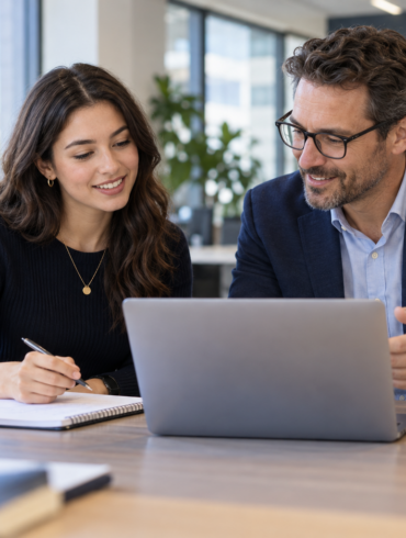 A new employee and mentor reviewing work together at an office desk.
