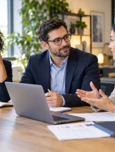 Three business professionals discussing hiring requirements at an office table.
